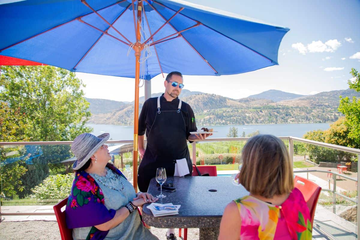 Chef John Burke shares a culinary creation with guests on the beautiful Blasted Church patio with a view of Skaha Lake