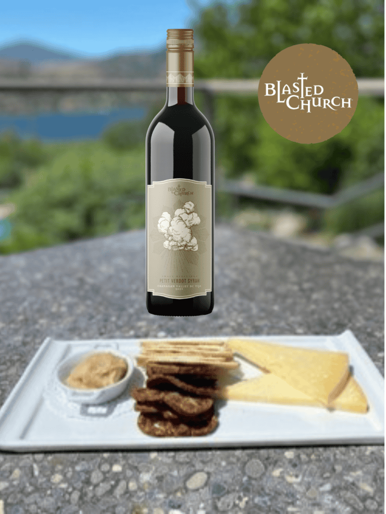 Petit Verdot Syrah 2023 sits on the Blasted Church patio table with a plate of cheese in the foreground