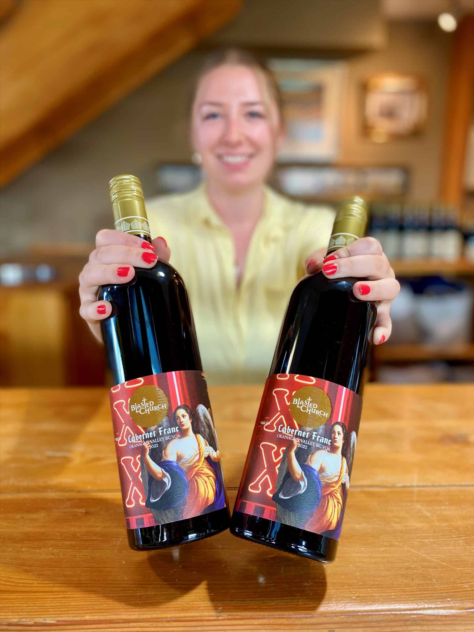 Kaylee holds two bottles of Blasted Church Cabernet Franc 2022 in the wine shop